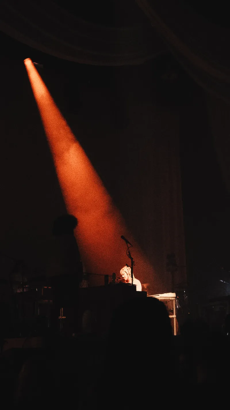 A single orange spotlight beam cutting through darkness onto a keyboard player on stage.