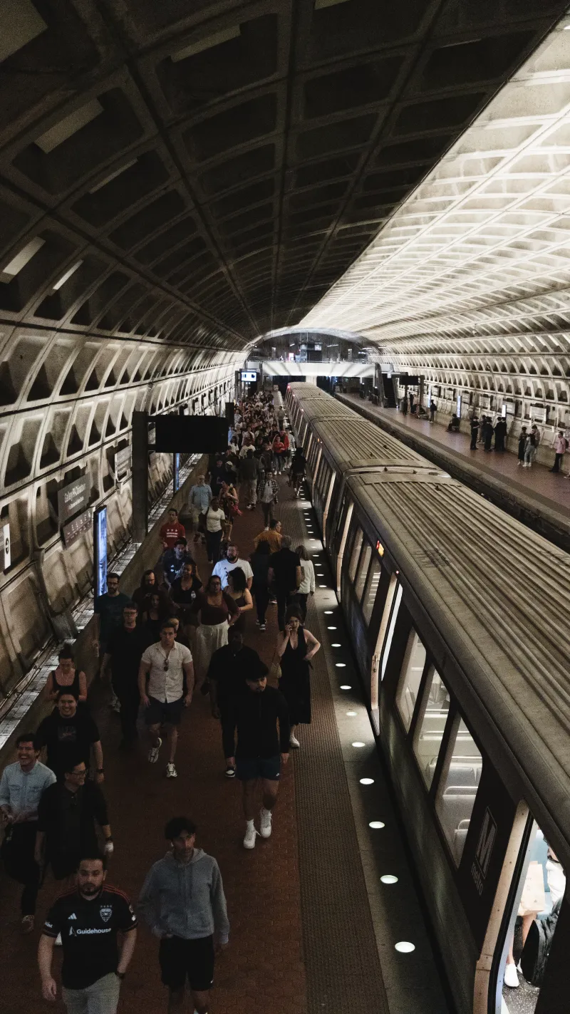 Crowds filling a curved, coffered metro platform as a train waits alongside.